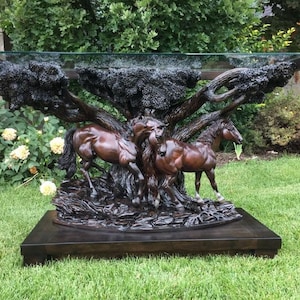 Puede incluir: Una mesa de centro de vidrio con una base de madera tallada que representa tres caballos corriendo por un bosque. La base es de color marrón oscuro y la tapa de vidrio es transparente.