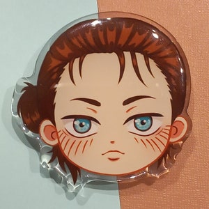 Peut inclure: Un charme en acrylique transparent repr&eacute;sentant un personnage de dessin anim&eacute; avec des cheveux bruns, des yeux bleus et une expression s&eacute;rieuse. Le personnage a un l&eacute;ger blush rose sur les joues.