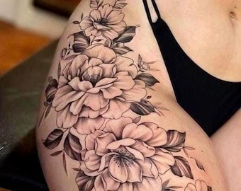 May include: A detailed tattoo design featuring large, blooming flowers and foliage in shades of gray and black. The floral arrangement cascades down the thigh, showcasing intricate shading and delicate petal details. The tattoo is a botanical-themed body art.