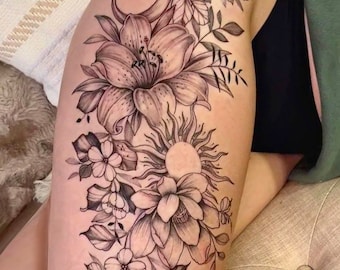May include: Black and white tattoo design of a crescent moon, sun, and various flowers on a person's leg.