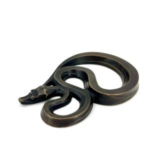 Op de afbeelding: Bronzen metalen slangensculptuur met een opgerold lichaam en gedetailleerde kop. De sculptuur staat op een witte achtergrond en toont het ontwerp en de textuur van de slang.