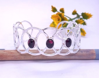 May include: A silver bangle bracelet with a delicate, openwork design featuring three round, dark red gemstones.