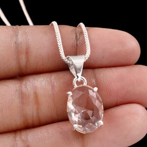 May include: A silver pendant necklace with an oval, faceted, clear gemstone. The gemstone is set in silver and suspended from a fine silver chain. The background is black.