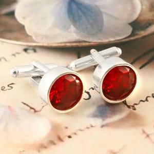 May include: A pair of silver cufflinks with red gemstone accents. The cufflinks are round and have a polished finish.