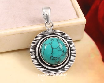 May include: A silver pendant with a turquoise stone set in a circular design. The pendant has a textured outer ring and a smooth inner ring.