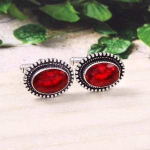 Peut inclure: Une paire de boutons de manchette en argent avec des pierres précieuses ovales rouges serties dans un cadre argenté décoratif.
