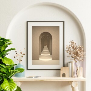 May include: A framed print of a hallway with a series of arches leading to a light at the end. The arches are a light brown color and the walls are a slightly darker brown. The floor is a light beige color.