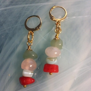 Peut inclure: Une paire de boucles d'oreilles créoles dorées avec un pendentif composé de quatre perles de pierres précieuses. Les perles sont vertes, roses, blanches et rouges.