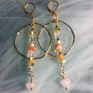 May include: Gold hoop earrings with a dangling chain of colorful gemstones, including pink, green, and blue, ending with a large pink gemstone.