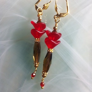 May include: A pair of dangle earrings featuring red glass flower-shaped beads and gold-toned metal accents.