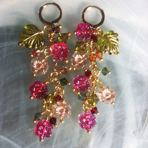 May include: Gold dangle earrings featuring pink, green and clear glass beads shaped like flowers and leaves.