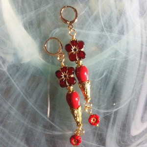 May include: A pair of gold earrings with red glass flower beads and gold accents. The earrings are dangling and have a teardrop shape.