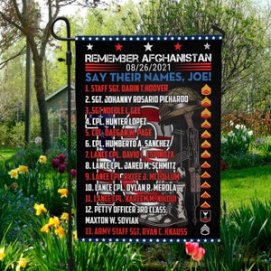 May include: A black garden flag with a white background and red stars. The flag features a soldier in a helmet and a rifle, with the text "Remember Afghanistan 08/26/2021 Say Their Names, Joe!" and a list of names and ranks.
