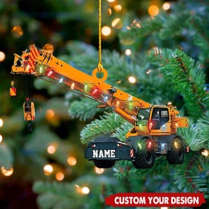 Può includere: Un ornamento per albero di Natale a forma di gru arancione con una serie di luci colorate. L'ornamento ha la scritta "NAME" sul davanti ed è appeso a un filo d'oro. Il testo "CUSTOM YOUR DESIGN" è in basso.