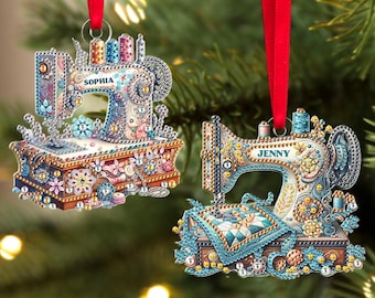 Puede incluir: Dos adornos navideños con forma de máquinas de coser, decorados con cuentas y pedrería de colores. El adorno superior dice "Sophia" y el adorno inferior dice "Jenny".