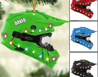 May include: A green motorcycle helmet ornament with a string of colorful lights and the name "DAVID" on the side. The helmet is decorated to look like a Christmas tree.