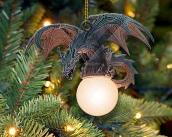 May include: A black and brown dragon ornament with outstretched wings, perched atop a white light bulb. The ornament is hanging from a gold string on a green Christmas tree.