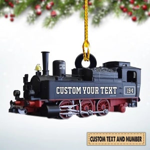 May include: Black and red model train ornament with the text "CUSTOM YOUR TEXT" and the number "194". The ornament is suspended by a gold string and is designed for customization. The ornament is a miniature replica of a steam engine.