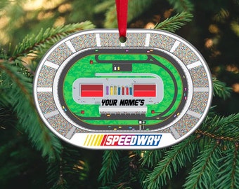 May include: Oval-shaped Christmas bauble featuring a detailed illustration of a race track with a green field and red, yellow, and blue cars. The bauble is white with a black outline and the text "YOUR NAME'S SPEEDWAY" printed on the bottom.