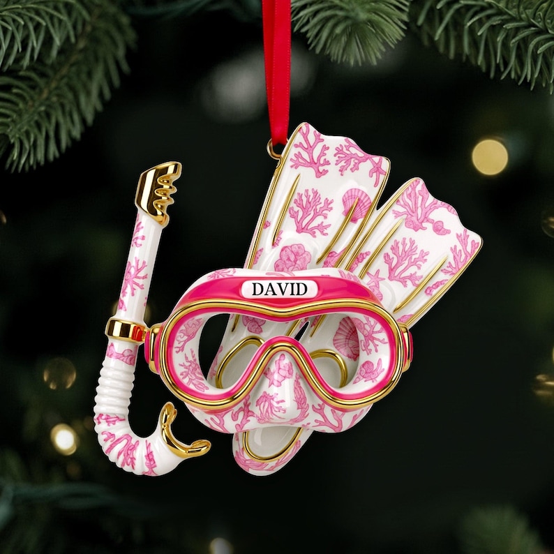 May include: A white and pink scuba diving ornament with gold accents, featuring a snorkel, mask, and fins. The mask has the name "DAVID" printed on it. The ornament is hanging from a red ribbon.
