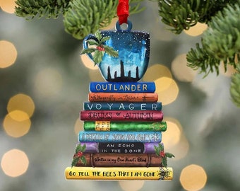 May include: A Christmas ornament shaped like a stack of books with a blue teacup on top. The books are from the Outlander series by Diana Gabaldon. The titles of the books are Outlander, Dragonfly in Amber, Voyager, Drums of Autumn, A Breath of Snow and Ashes, An Echo in the Bone, Written in My Own Heart's Blood, and Go Tell the Bees That I Am Gone.