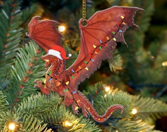 May include: A red dragon Christmas ornament with a Santa hat and string lights. The dragon has large wings and is hanging from a gold string. The ornament is hanging on a green Christmas tree.