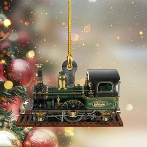 May include: A green and black model train ornament with gold accents. The train has a black caboose with a window and the name "Johnson" on the side. The ornament is hanging from a gold string.
