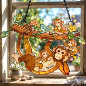 May include: A decorative stained glass window hanging featuring a family of monkeys. The monkeys are brown and tan, hanging from a brown branch with green leaves and orange flowers. The names "Tom", "Anna", "David", and "Mommy" are written on the monkeys.
