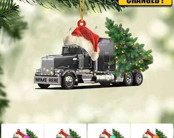 May include: A black semi-truck with a Christmas tree in the back and a Santa hat on the cab. The truck has lights on it and the text "NAME HERE" on the front bumper. The truck is a Christmas ornament.