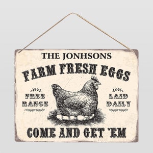 Op de afbeelding: Een rechthoekig bord in vintage stijl met een touwhanger. Het bord toont de tekst "THE JONHSONS FARM FRESH EGGS" boven een gedetailleerde illustratie van een kip op een nest met eieren. Extra tekst is onder meer "FREE RANGE" en "LAID DAILY".