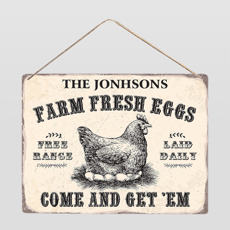 Op de afbeelding: Een rechthoekig bord in vintage stijl met een touwhanger. Het bord toont de tekst "THE JONHSONS FARM FRESH EGGS" boven een gedetailleerde illustratie van een kip op een nest met eieren. Extra tekst is onder meer "FREE RANGE" en "LAID DAILY".