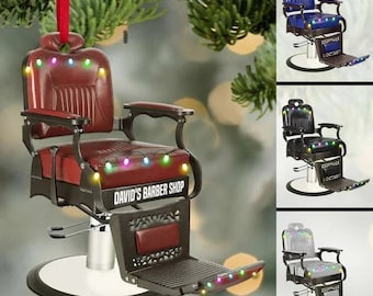 Puede incluir: Una silla de barbero roja con un marco de metal negro y una base blanca. La silla tiene un letrero que dice "David's Barber Shop" y está decorada con luces navideñas de colores.