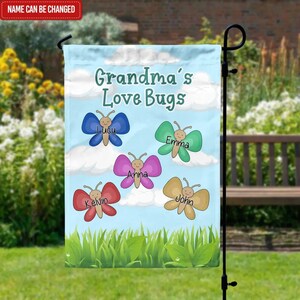 May include: A colorful garden flag with the text "Grandma's Love Bugs" and five butterflies with names written on them. The butterflies are blue, green, pink, red, and yellow.