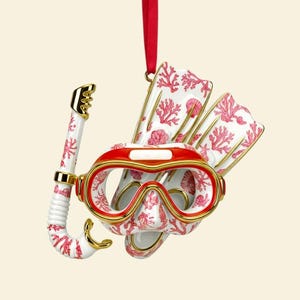 May include: A decorative Christmas ornament featuring a snorkel, mask, and fins. The white ceramic pieces are adorned with a coral reef pattern in red. The mask has a red frame with gold accents, and a red ribbon for hanging.