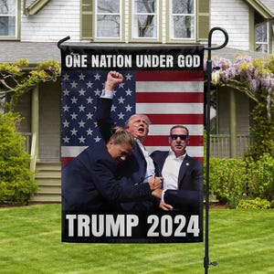 May include: A black and white garden flag with an American flag background. The flag features three people, two men and one woman, with the text "ONE NATION UNDER GOD" and "TRUMP 2024".