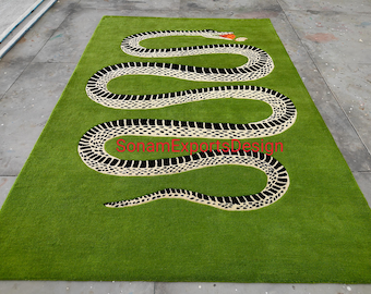 Puede incluir: Una alfombra rectangular verde con un gran diseño de serpiente. La serpiente está representada en blanco y negro, con un patrón detallado. La cabeza de la serpiente está en la parte superior, con un acento rojo y naranja. La alfombra tiene el texto "Sonam Exports Design".