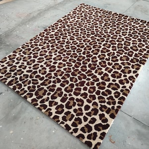 Puede incluir: Alfombra rectangular con estampado de leopardo. La alfombra presenta un diseño repetido de manchas marrones y beige sobre un fondo crema. La alfombra está hecha de un material suave y es adecuada para una sala de estar o dormitorio, mide aprox. 180 cm x 120 cm.