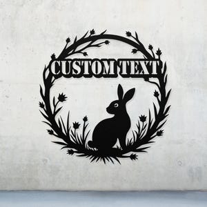 May include: Black metal silhouette of a rabbit sitting in a wreath of stylized leaves and flowers. The wreath has the text "CUSTOM TEXT" in the center.