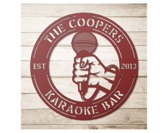 May include: A red metal sign with the words "THE COOPERS KARAOKE BAR" encircling a hand holding a microphone. The sign also includes the year "2013" and the word "EST". The sign is set against a light wood background.