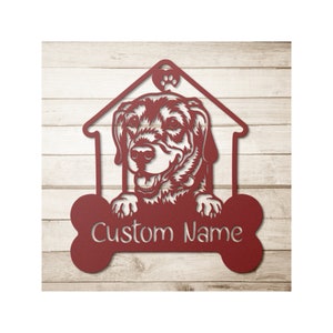 May include: A red metal dog house sign featuring a dog's face, a paw print, and a bone-shaped area for a custom name. The sign is designed to be mounted on a wall and is made of metal.