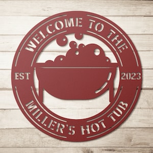 May include: A circular, red metal sign with the words "WELCOME TO THE MILLER'S HOT TUB" cut out. The sign features a hot tub graphic with bubbles and the year "2023". The word "EST" is also cut out.