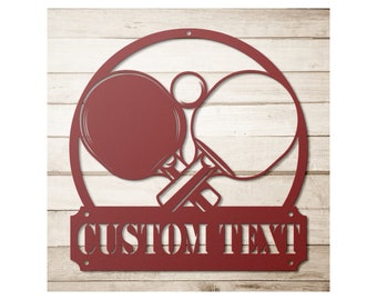 May include: Red metal wall decor featuring two crossed ping pong paddles with a ball in the center. The decor has a rounded top and a rectangular base with the text "CUSTOM TEXT" in white.