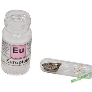 Puede incluir: Un pequeño vial de vidrio que contiene una muestra de Europio, un elemento metálico blanco plateado. El vial está etiquetado con el símbolo del elemento "Eu" y el número atómico 63. La etiqueta también dice "Europio".