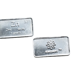 Op de afbeelding: Twee zilveren staven, een met het chemische symbool Zn voor zink, de tekst "Zink 99,99% 1 gram" en het nummer 30, en de andere met een atoomsymbool en de tekst "Moments in Time".