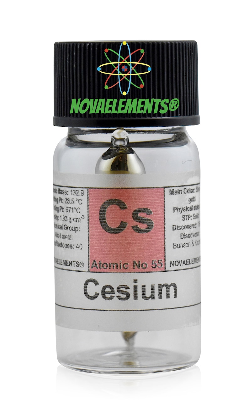 Op de afbeelding: Een doorzichtige glazen fles met een zwarte dop die een klein monster cesium bevat, een zacht, zilverkleurig-gouden alkalimetaal. Het etiket vermeldt "Cesium, atoomnummer 55" en bevat informatie over de eigenschappen van het element.