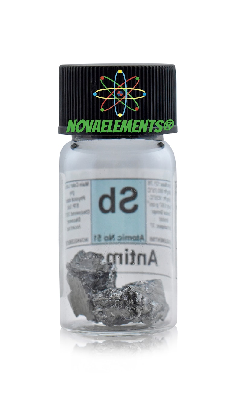 Pu&ograve; includere: Un piccolo flacone di vetro con un tappo nero che contiene un campione di Antimonio, un metalloide grigio argenteo. L'etichetta sul flacone riporta "Antimonio" e "Numero atomico 51" con il simbolo chimico "Sb". Il flacone ha un logo Novaelements sul tappo.
