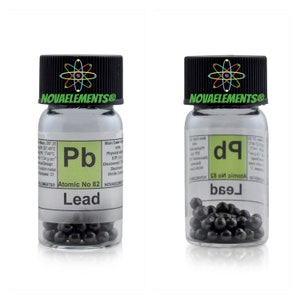 Puede incluir: Una botella de vidrio transparente con tapa negra que contiene pequeñas bolitas de plomo negras. La etiqueta de la botella dice "Pb Atomic No 82 Lead" y "NOVAELEMENTS®".