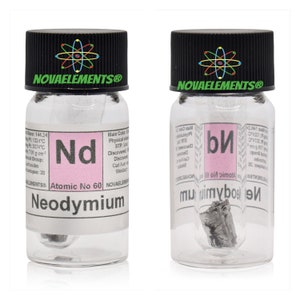 Puede incluir: Una botella de vidrio transparente con tapa negra que contiene un pequeño trozo de metal de neodimio. La etiqueta de la botella dice "Neodimio" y "Número atómico 60".