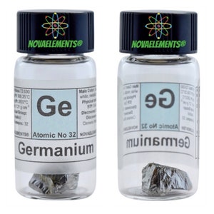 Op de afbeelding: Twee doorzichtige glazen flessen met zwarte deksels die een klein monster Germanium bevatten, een zilvergrijs metalloïde element. De flessen hebben een wit etiket met het symbool van het element "Ge", het atoomnummer "32" en de naam "Germanium".
