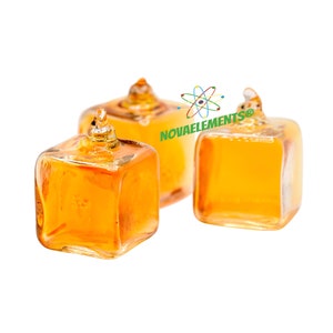 May include: Three small, clear glass bottles with a square shape and a pointed top. The bottles are filled with a golden liquid.
